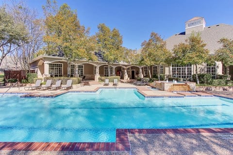 Stunning, tree-lined swimming pool with tanning deck and lounge seating